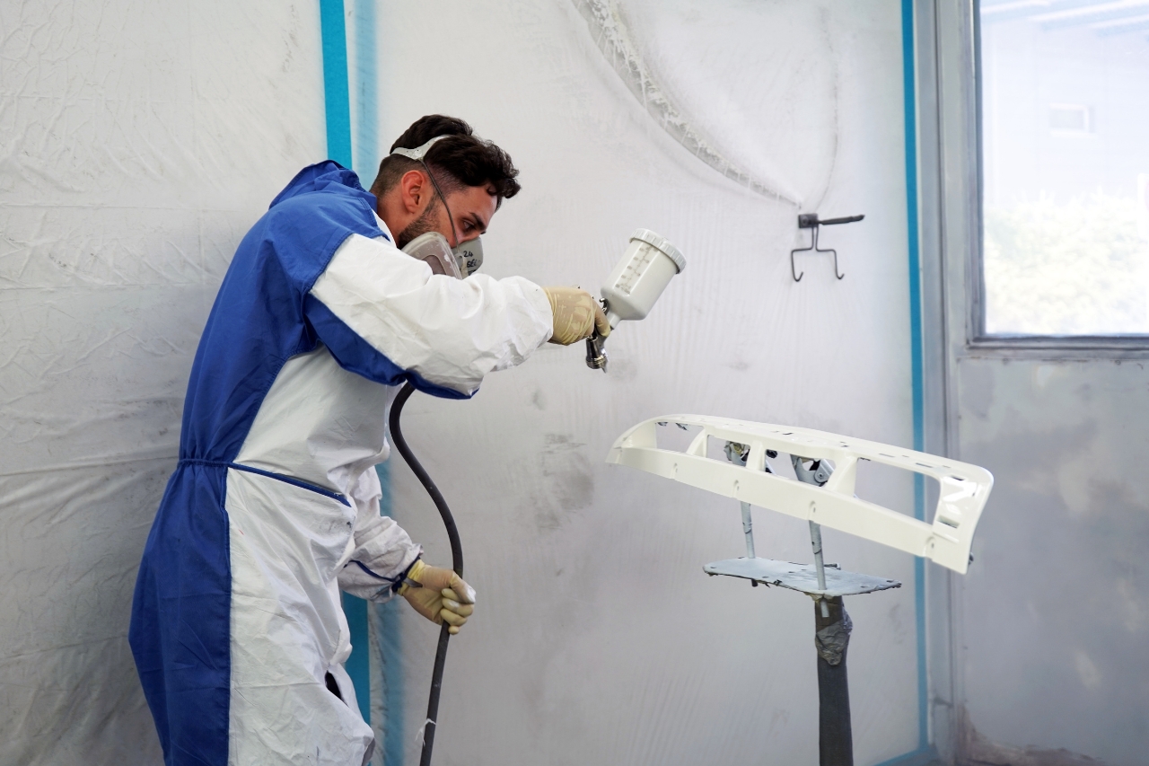 Lackierer von Lucky Cars trägt in der Spritzkabine weißen Lack auf Fahrzeugteil auf – präzise Lackierung und professionelle Autolackierung als Teil des Autoreparaturservice in Winterthur.