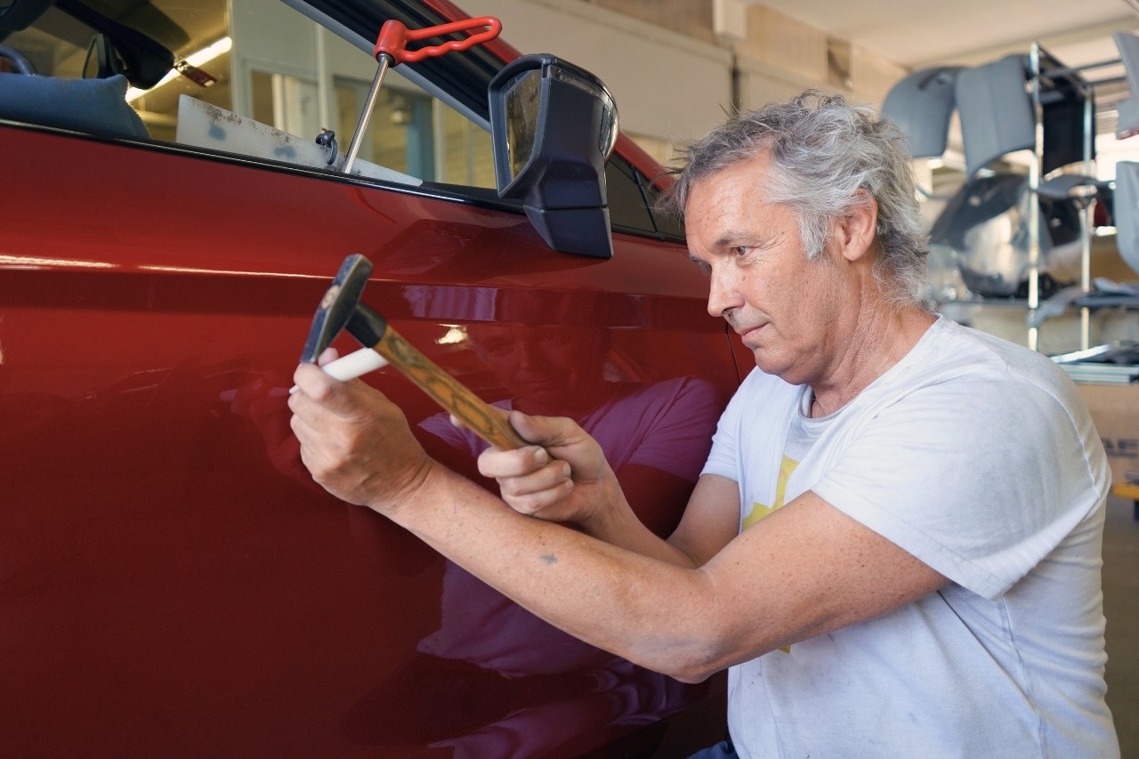 Karosseriebauer von Lucky Cars bearbeitet Delle an rotem Fahrzeug mit Hammer – präzise Unfallreparatur ohne Lackierung im Rahmen des Auto Reparaturservice in Winterthur.